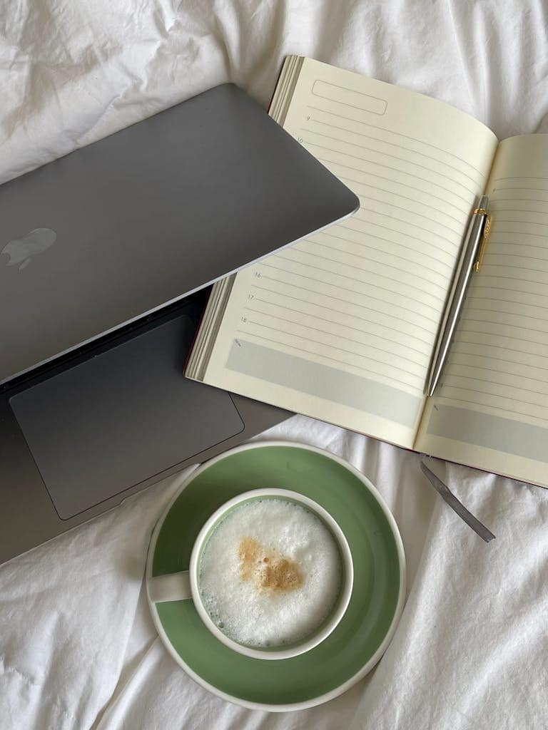 A laptop and coffee cup on a bed